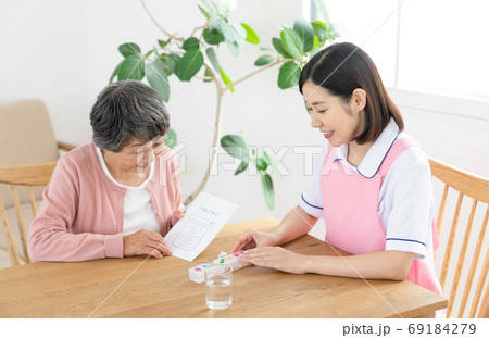 薬ケースの説明をする介護士 69184279