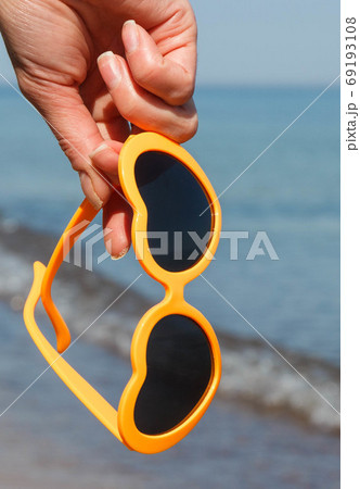 Hand of woman with sunglasses in shape of heart on beach. Summer time 69193108