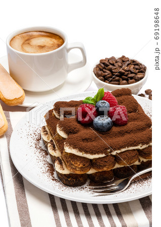 portion of Classic tiramisu dessert with raspberries, blueberries and cup of fresh hot espresso isolated on white background - clipping path 69198648