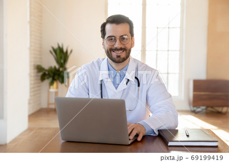 Head shot portrait smiling doctor wearing glasses working on laptop 69199419