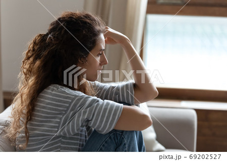 Sad young woman sitting on couch feels depressed side view Sad young woman sitting on couch feels depressed side view 69202527