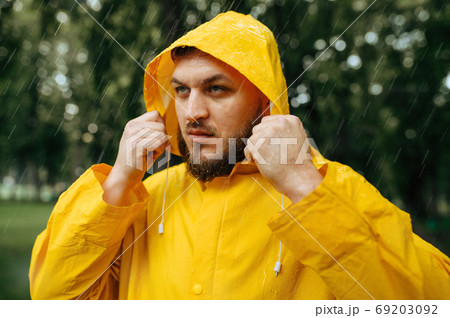 Man in raincoat puts on a hood in rainy day 69203092