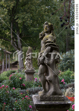 An old statue of a goddess stands in a botanical garden in Rothenburg ob der Tauber, covered with green moss, among the flowers. 69204696