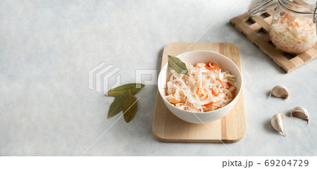 White ceramic bowl with homemade appetizer sauerkraut on a light, concrete background. Glass jar and spices garlic and bay leaf. Close up with copy space White ceramic bowl with homemade appetizer sauerkraut on a light, concrete background. Glass jar and spices garlic and bay leaf. Close up with copy space 69204729