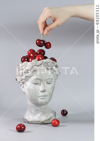 Stylish decoration made in shape of Greek goddess head full of red ripe cherries. Beautiful design elements. Gray background. 69205311