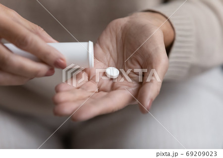 Close up mature woman taking out pill from plastic bottle 69209023