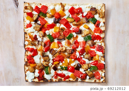 Tasty traditional Tarte Flambee from the Alsace region of France with a thin pastry crust topped with creme fraiche or cheese, onions, herbs, lardons and tomato sliced ready to serve as an appetizer 69212012