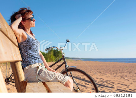 Middle-aged woman came on a Bicycle to the beach and resting sit Middle-aged woman came on a Bicycle to the beach and resting sit 69212191