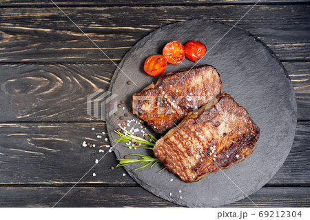 juicy piece of fried meat lies on a stone plate against a black wooden table 69212304