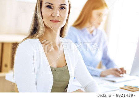 Business woman portrait at sunny office. Businesspeople or colleagues discussing something at meeting while sitting at the desk in office. Casual clothes style. Audit, tax or lawyer concept Business woman portrait at sunny office. Businesspeople or colleagues discussing something at meeting while sitting at the desk in office. Casual clothes style. Audit, tax or lawyer concept 69214397