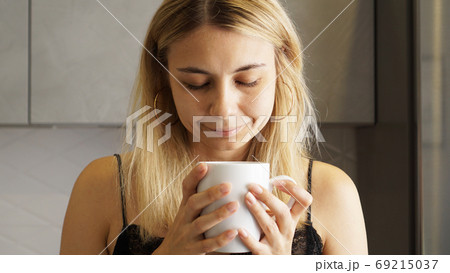 Close up of a woman taking in smell of coffee with her eyes closed Close up of a woman taking in smell of coffee with her eyes closed 69215037