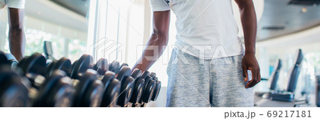 African American man picking up a dumbbell from the rack and looking outside at gym 69217181