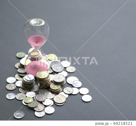 Hourglass with sand flowing and coins on table. 69218521