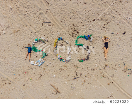 SOS lettering and mom and son sunbathe on the beach nearby. Environmental problem. Ecology concept. Plastic on the beach with sos writing. Spilled garbage on the beach 69223029