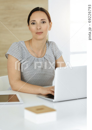Cheerful smiling businesswoman working with computer while sitting at the desk in sunny office. Middle aged female lawyer or auditor at work Cheerful smiling businesswoman working with computer while sitting at the desk in sunny office. Middle aged female lawyer or auditor at work 69226793