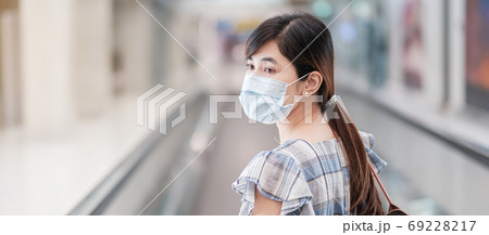 Young adult female wearing face mask in airport terminal, protec 69228217
