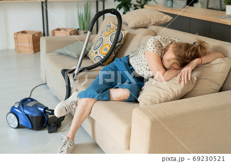 Mature exhausted blond female lying on soft pillows on couch while having rest 69230521