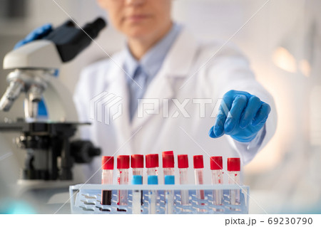 Gloved hand of laboratory worker in whitecoat taking small flask with blood test 69230790