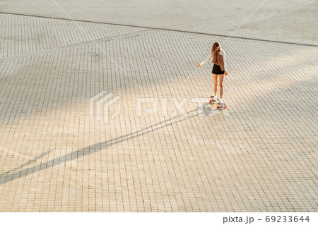 Young woman rides a skateboard under the sunset. Young woman rides a skateboard under the sunset. 69233644