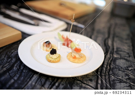 4 small canapes are placed on a white round plate. The table surface is a marble pattern. Selective and blurred focus. 69234311