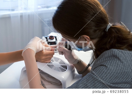 Woman manicurist cleaning pterygium near cuticle using apparatus for manicure. Woman manicurist cleaning pterygium near cuticle using apparatus for manicure. 69238055