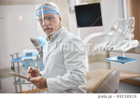 Competent dental specialist taking notes at work Competent dental specialist taking notes at work 69238919