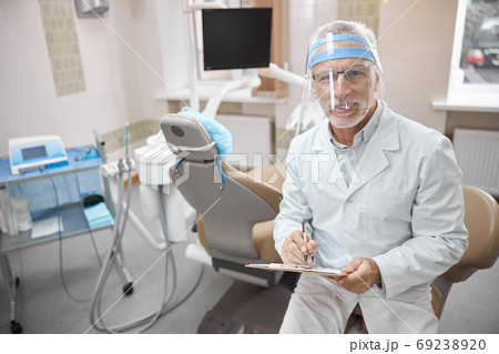 Friendly dentist holding a clipboard while working in clinic 69238920