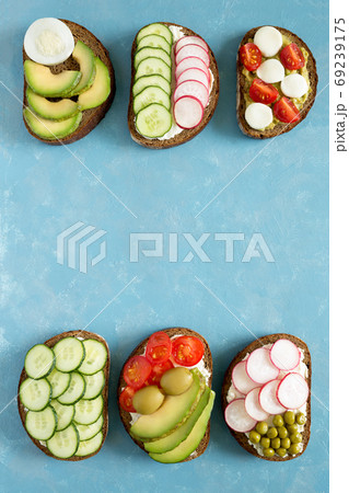 Few homemade sandwiches with vegetables cucumbers, radishes, avocado on slices of dark bread. Diet, vegetarian food on a bright blue background. Flat lay, top view, place for text. 69239175