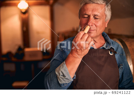 Handsome winemaker enjoying the scent of wine cork 69241122