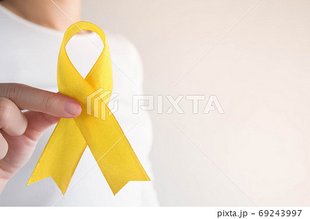 Young female holding yellow gold ribbon awareness symbol for endometriosis, suicide prevention, sarcoma bone cancer, bladder cancer, liver cancer and childhood cancer concept. Health care. Copy space. 69243997