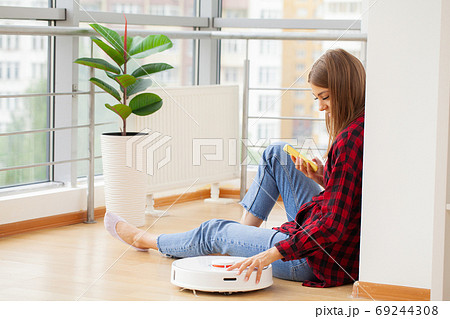 Woman turns on smart robot vacuum cleaner 69244308