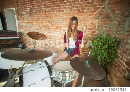 Woman recording music, singing and playing drums while sitting in loft workplace or at home 69245555