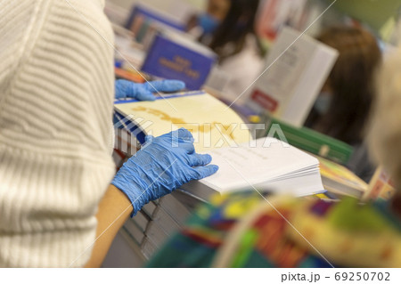 Unrecognizable girl in protective blue protective medical gloves reads a book in a bookstore. Healthcare concept, quarantine, personal protection Unrecognizable girl in protective blue protective medical gloves reads a book in a bookstore. Healthcare concept, quarantine, personal protection 69250702