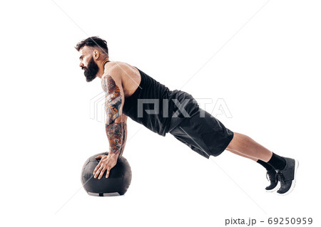 Muscular tattooed bearded male exercising fitness weights Medicine Ball push ups exercises in studio isolated on white background Muscular tattooed bearded male exercising fitness weights Medicine Ball push ups exercises in studio isolated on white background 69250959