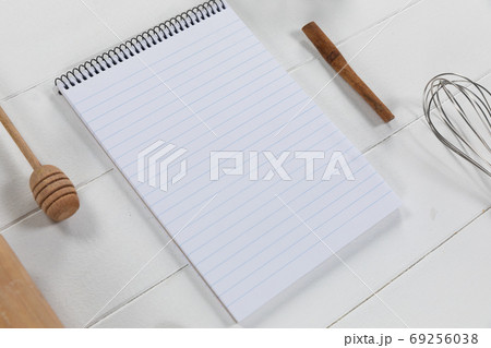 View of a composition with a notebook with wooden spoon and whisker on white wooden surface 69256038