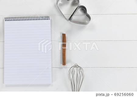 View of a composition with a notebook with cookie cutters and whisker on white wooden surface View of a composition with a notebook with cookie cutters and whisker on white wooden surface 69256060