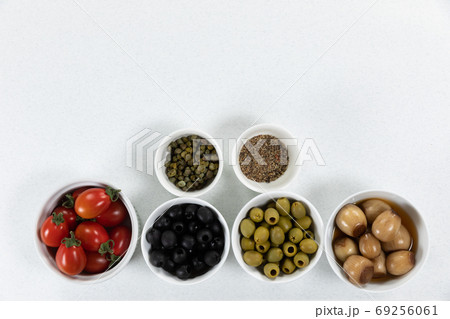 View of a six bowls with fresh tomatoes, olives, nuts and seasoning on plain white surface View of a six bowls with fresh tomatoes, olives, nuts and seasoning on plain white surface 69256061