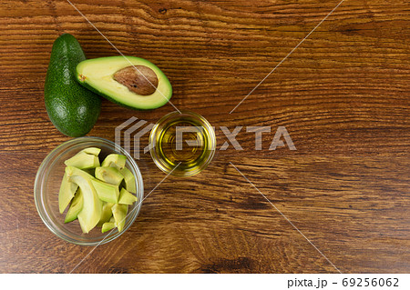 View of two avocados, olive oil bottle and cut avocado in a bowl on wood table background 69256062