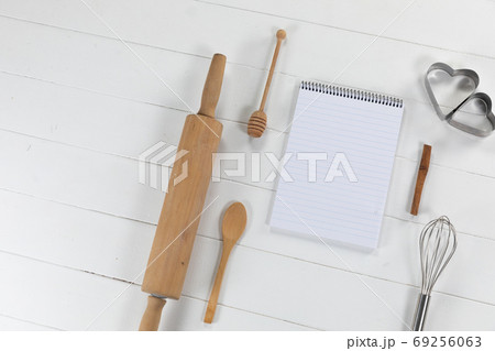View of a composition of a notebook with cookie cutters, whisker and rolling pin on white surface View of a composition of a notebook with cookie cutters, whisker and rolling pin on white surface 69256063