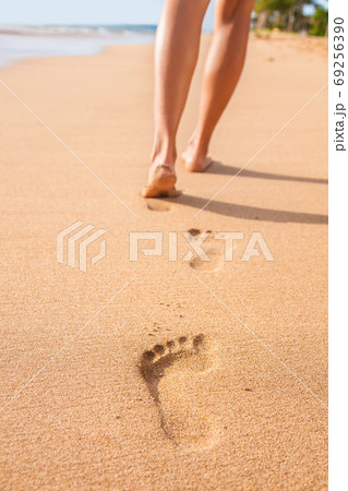 Beach sand footprints woman feet walking barefoot. Travel girl relaxing walking on golden sand beach leaving footprints in the sand. Closeup detail of female feet and legs at sunset. 69256390