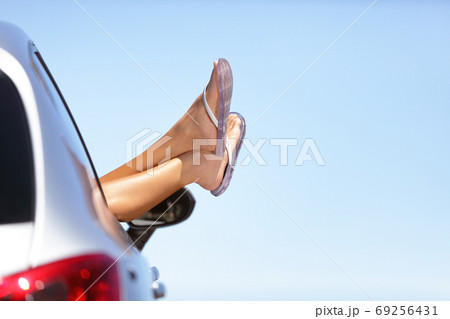 Summer road trip car vacation fun. Woman legs out the car window in blue sky background. Carefree, freedom, road trip travel and holidays copy space. Woman relaxing feet in flip flops lifestyle. Summer road trip car vacation fun. Woman legs out the car window in blue sky background. Carefree, freedom, road trip travel and holidays copy space. Woman relaxing feet in flip flops lifestyle. 69256431