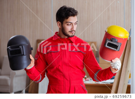 Young repairman with a welding gun electrode and a helmet weldin Young repairman with a welding gun electrode and a helmet weldin 69259673