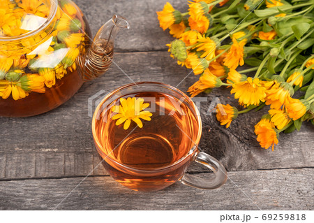 Cup of herbal tea and transparent teapot and marigold flowers on wood background. Calendula Tea Benefits Your Health concept 69259818