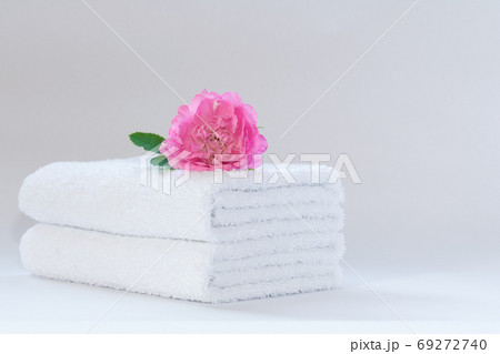 Two white neatly folded terry towels with a rose flower on a light background. 69272740
