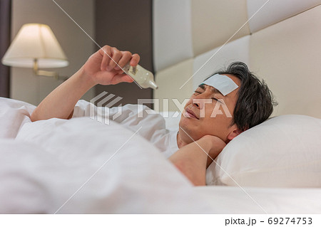 夜、体温計で熱を測る若い男性 69274753