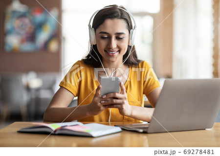 Young girl student sitting at cafe, using laptop and smartphone 69278481
