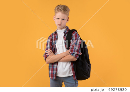 Upset male pupil holding arms crossed on pastel orange wall 69278920