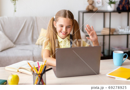 Girl sitting at desk, using laptop and waving at camera Girl sitting at desk, using laptop and waving at camera 69278925