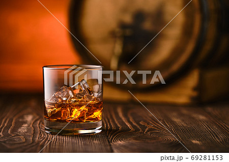 Glass of whiskey with ice with barrel on background 69281153