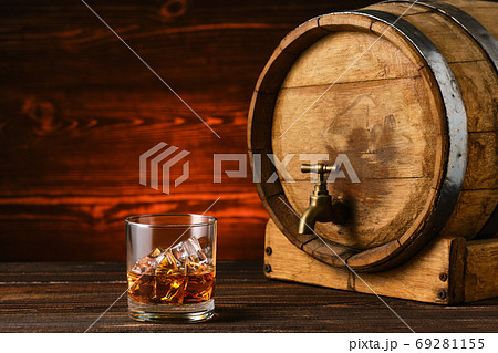 Glass of whiskey with ice near wooden barrel 69281155